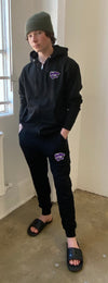Model wearing a beanie and the black hoodie and jogger set - both embroidered with purple powercat